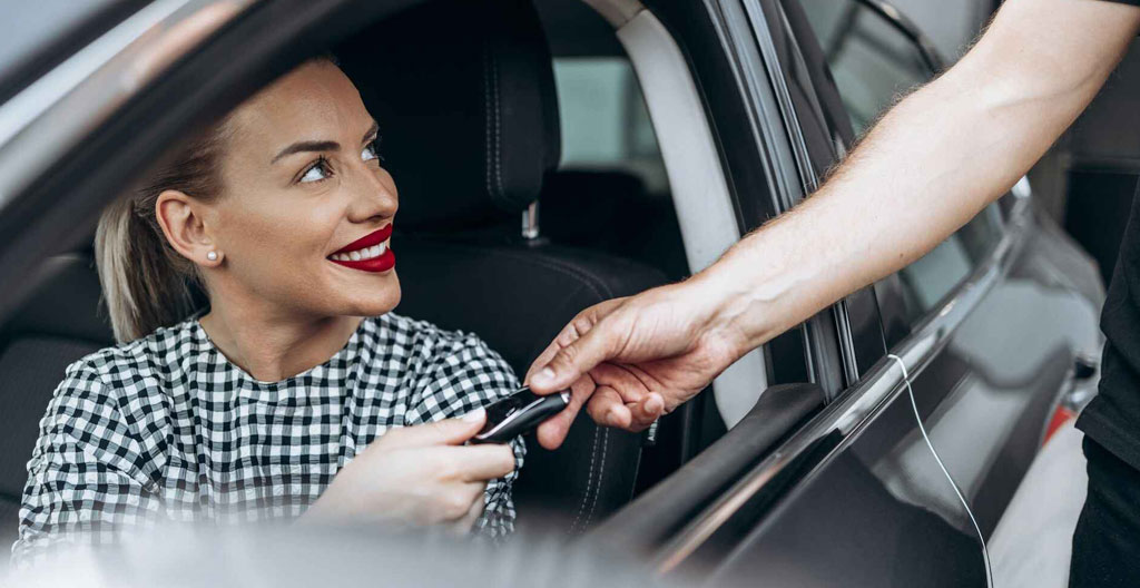 Professionnel au volant d'une berline de location garée sur parking de zone d'activité, consultant son planning de rendez-vous sur smartphone
