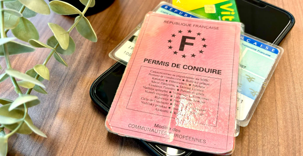 Professionnel consultant une réservation de véhicule sur tablette, avec permis de conduire et documents d'identité français disposés sur le bureau